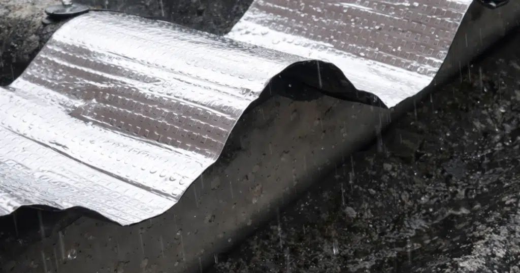 Cinta asfáltica impermeabilizante Texsatape de Texsa aplicada en tejado ondulado bajo lluvia, con terminación de foil aluminio expuesto al sol y a la intemperie